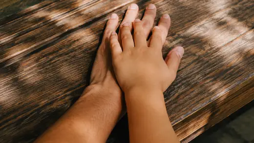 縁側の木の床で、大人の手に子どもの手が重なっている写真。